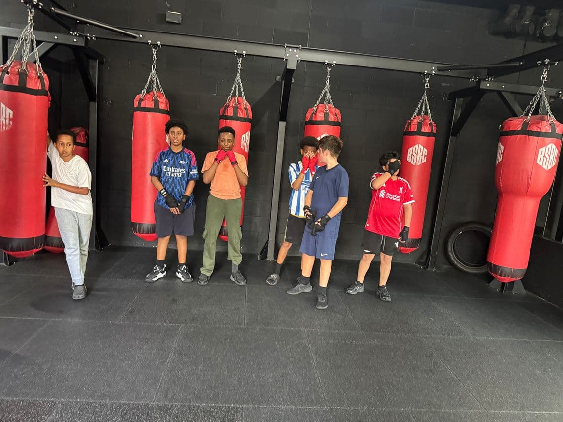 Young boxers standing in front of a row of red punch bags in a boxing gym