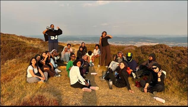 Young women sitting together on a hilltop in Wales at sunset